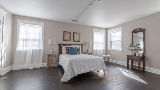 bedroom with multiple windows, dark hardwood / wood-style floors, and track lighting