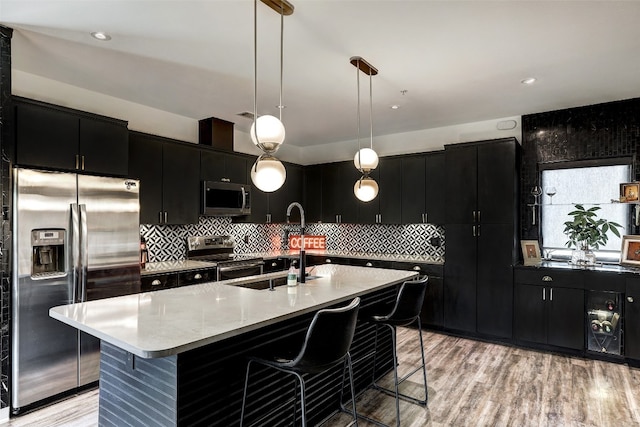 kitchen featuring a kitchen breakfast bar, light hardwood / wood-style flooring, a kitchen island with sink, hanging light fixtures, and stainless steel appliances