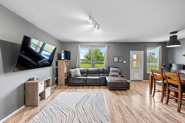 living room with a textured ceiling, rail lighting, and light wood-type flooring