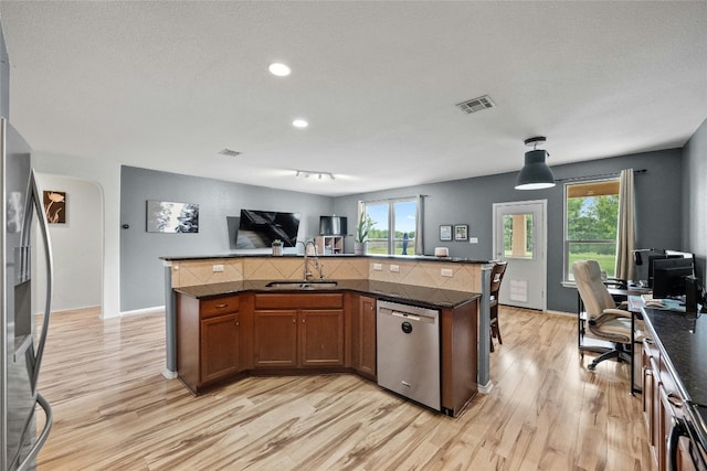 kitchen with light hardwood / wood-style flooring, decorative light fixtures, stainless steel appliances, sink, and a kitchen island with sink