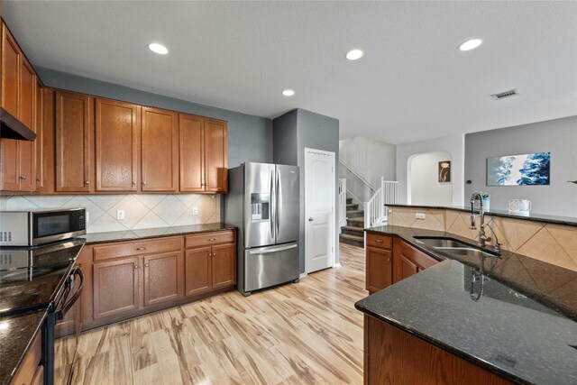 kitchen with dark stone counters, backsplash, sink, appliances with stainless steel finishes, and light hardwood / wood-style floors