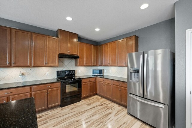 kitchen featuring appliances with stainless steel finishes, light hardwood / wood-style flooring, backsplash, and dark stone counters