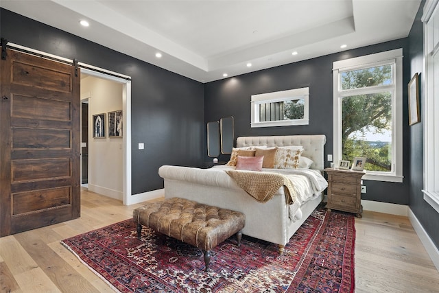 bedroom featuring a barn door, a raised ceiling, and light hardwood / wood-style flooring