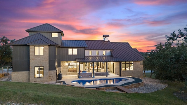 back house at dusk featuring a patio area, a yard, and an in ground hot tub