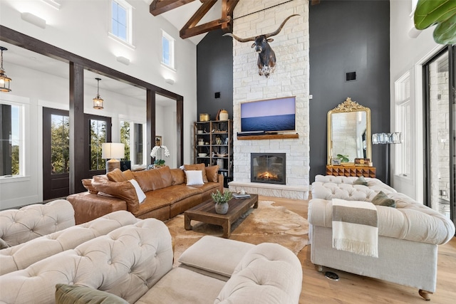 living room with high vaulted ceiling, beamed ceiling, a stone fireplace, and light wood-type flooring