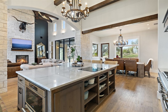 kitchen with hanging light fixtures, a center island, an inviting chandelier, a stone fireplace, and beam ceiling