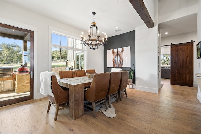 dining area featuring a barn door, a chandelier, light hardwood / wood-style floors, and a healthy amount of sunlight