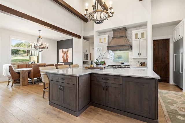 kitchen featuring light hardwood / wood-style flooring, custom range hood, a notable chandelier, light stone counters, and white cabinets