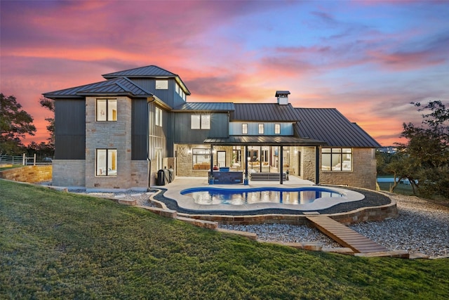 back house at dusk with a patio area, a yard, and a hot tub