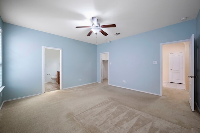 unfurnished bedroom featuring ensuite bath, light colored carpet, a walk in closet, a closet, and ceiling fan