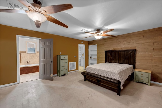 bedroom with ceiling fan, wood walls, and ensuite bath