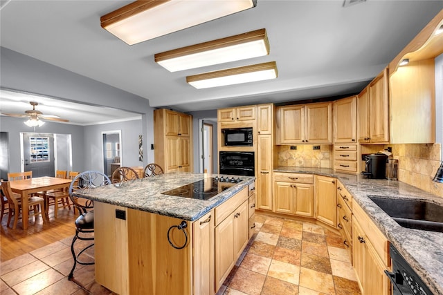 kitchen with a kitchen island, black appliances, a breakfast bar, ceiling fan, and light stone counters