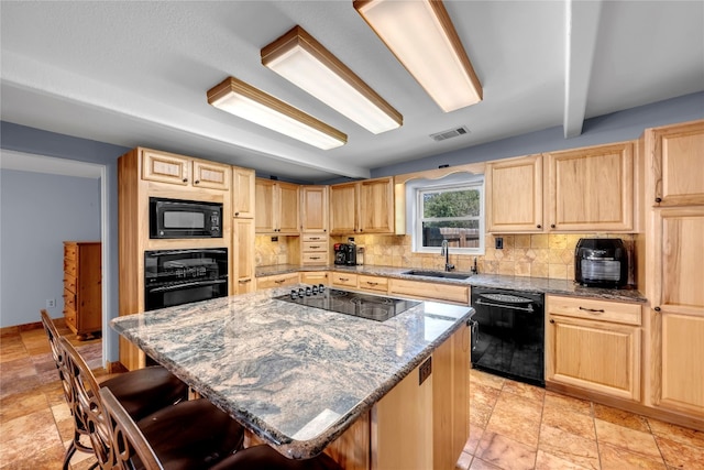 kitchen with a kitchen bar, light stone countertops, sink, black appliances, and a kitchen island