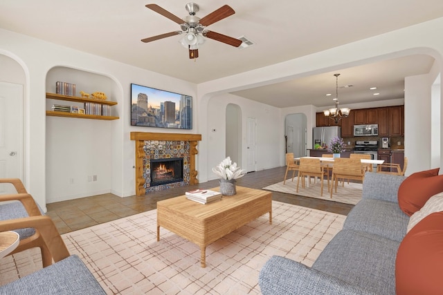 living room with light tile patterned flooring, a stone fireplace, and ceiling fan with notable chandelier