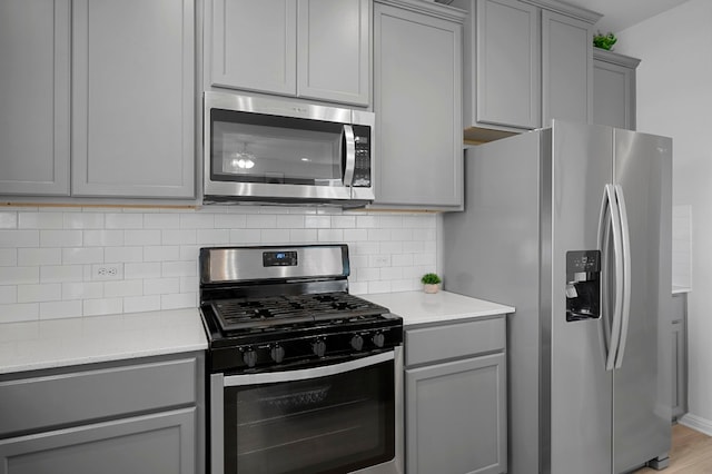 kitchen featuring gray cabinets, decorative backsplash, stainless steel appliances, and light hardwood / wood-style floors