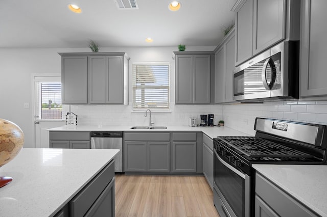 kitchen with appliances with stainless steel finishes, sink, gray cabinets, light stone counters, and light wood-type flooring