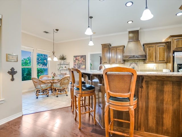 kitchen with crown molding, light stone counters, light hardwood / wood-style floors, premium range hood, and a breakfast bar