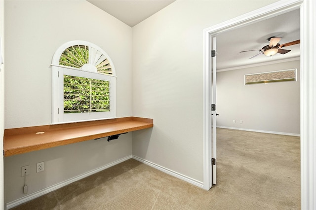 unfurnished office featuring built in desk, ceiling fan, and light carpet