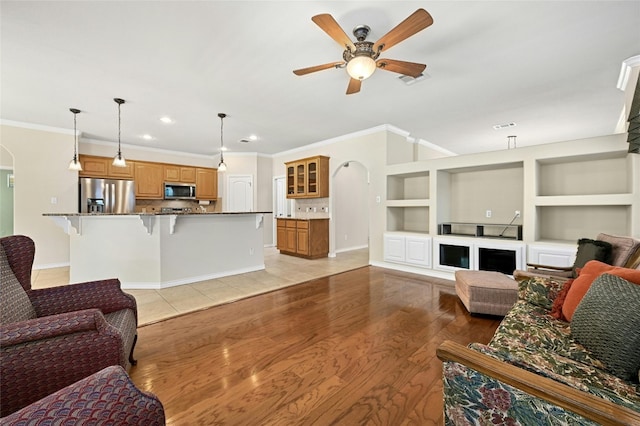 living room with light wood-type flooring, ornamental molding, and ceiling fan