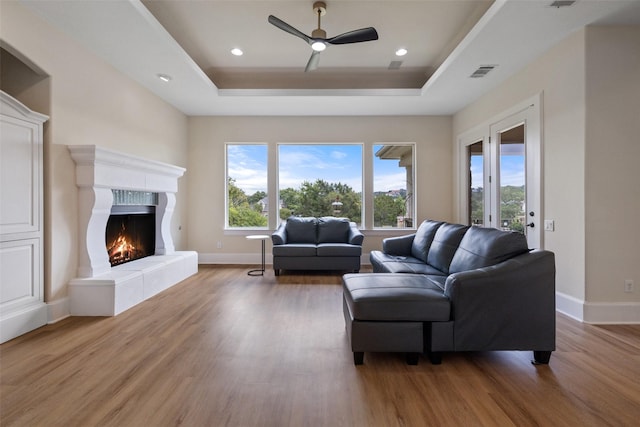 living room with hardwood / wood-style flooring, a tile fireplace, and a raised ceiling