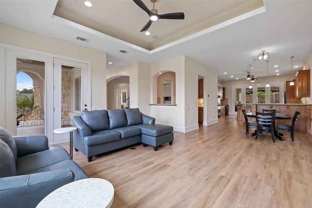 living room with ceiling fan, a tray ceiling, and light wood-type flooring