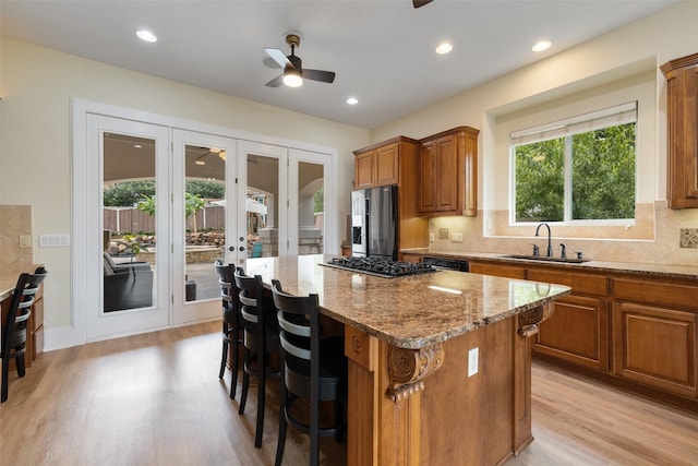 kitchen with a kitchen island, appliances with stainless steel finishes, sink, light stone countertops, and french doors