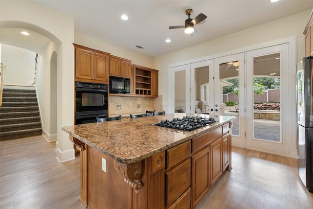 kitchen with a kitchen island, backsplash, light stone counters, black appliances, and light hardwood / wood-style flooring