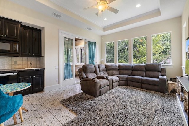 living room featuring a raised ceiling, crown molding, sink, and ceiling fan