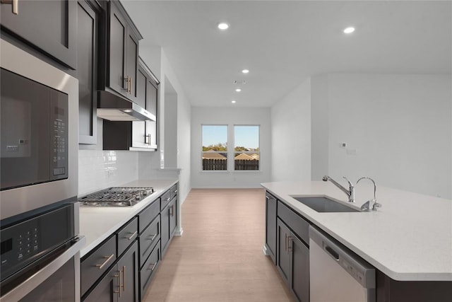 kitchen featuring tasteful backsplash, an island with sink, sink, stainless steel appliances, and light hardwood / wood-style flooring