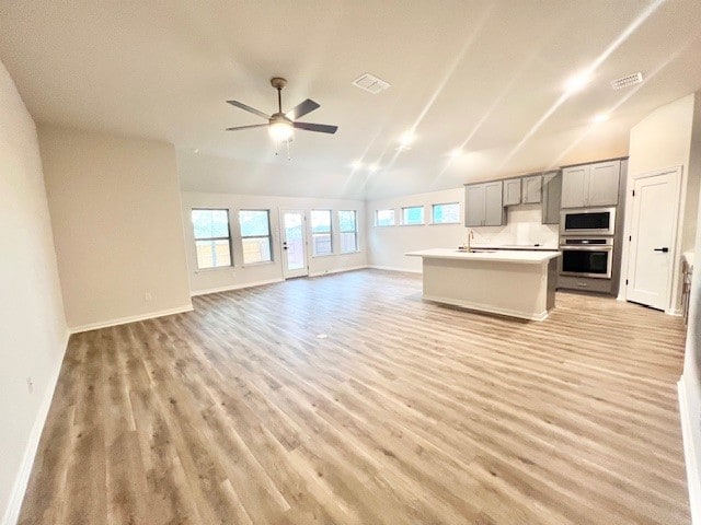 kitchen featuring lofted ceiling, light hardwood / wood-style flooring, an island with sink, gray cabinets, and appliances with stainless steel finishes