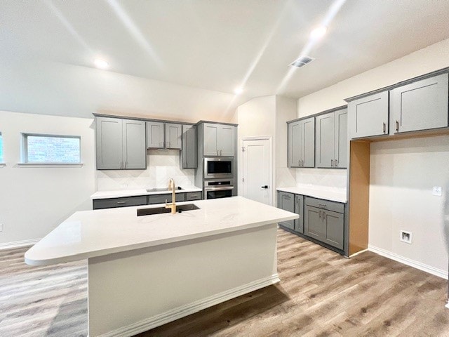 kitchen with gray cabinetry, sink, an island with sink, and stainless steel appliances