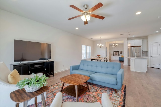 living room featuring light hardwood / wood-style flooring, sink, and ceiling fan with notable chandelier