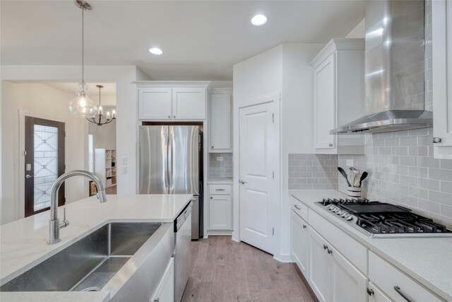 kitchen with white cabinetry, light hardwood / wood-style flooring, sink, appliances with stainless steel finishes, and wall chimney range hood