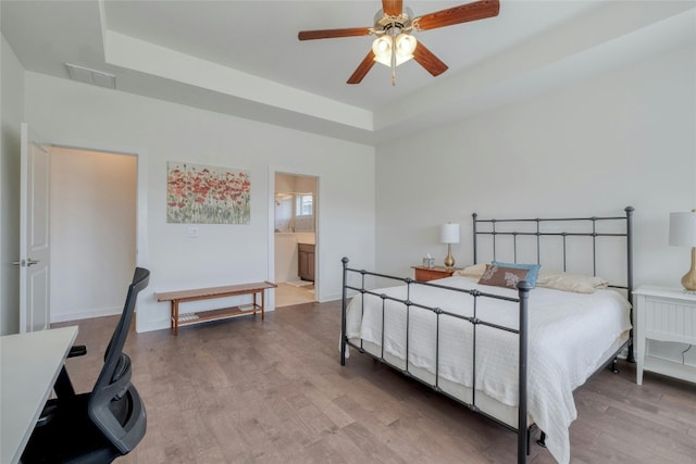 bedroom featuring ceiling fan, hardwood / wood-style flooring, a raised ceiling, and ensuite bath