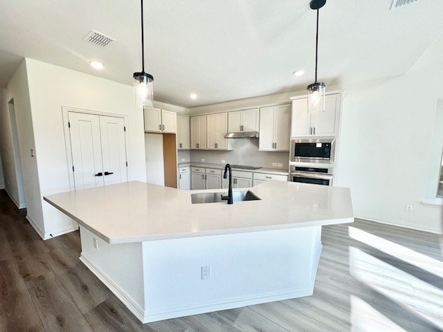 kitchen with white cabinets, a large island with sink, hanging light fixtures, and sink