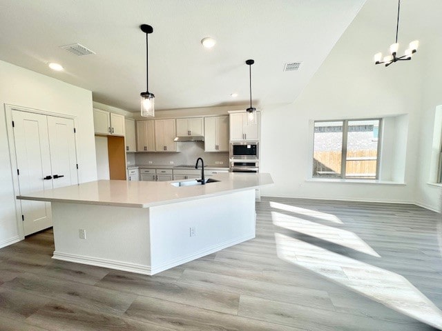 kitchen with white cabinetry, decorative light fixtures, and an island with sink