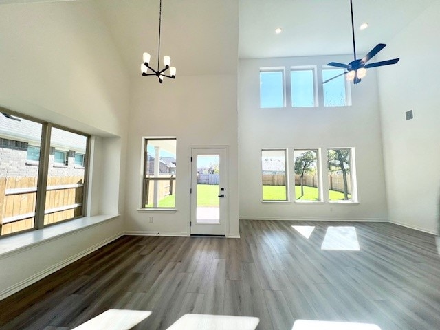 unfurnished living room featuring a high ceiling, hardwood / wood-style floors, and ceiling fan with notable chandelier