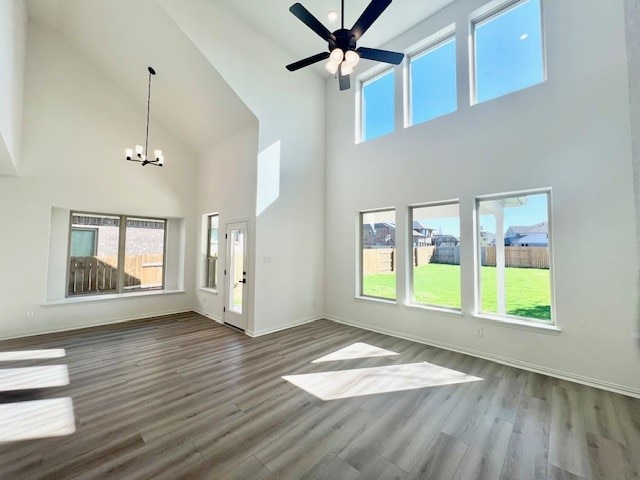 unfurnished living room featuring ceiling fan with notable chandelier, hardwood / wood-style flooring, and a high ceiling