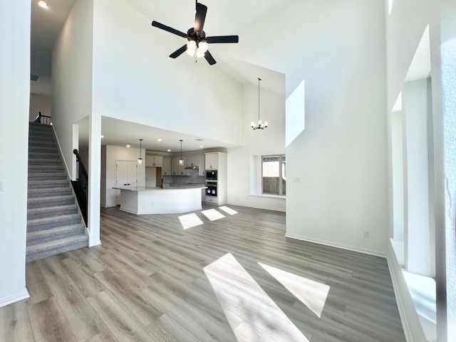 unfurnished living room featuring high vaulted ceiling, ceiling fan with notable chandelier, and light wood-type flooring