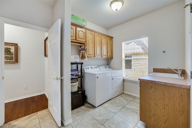 laundry area featuring a textured ceiling, cabinets, washing machine and clothes dryer, and sink