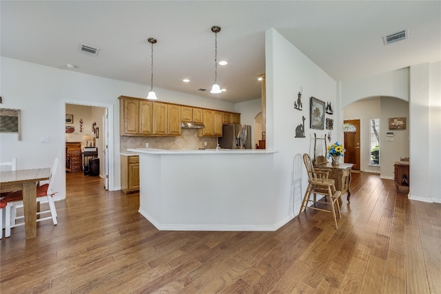 kitchen featuring decorative light fixtures, light hardwood / wood-style flooring, stainless steel fridge with ice dispenser, tasteful backsplash, and kitchen peninsula