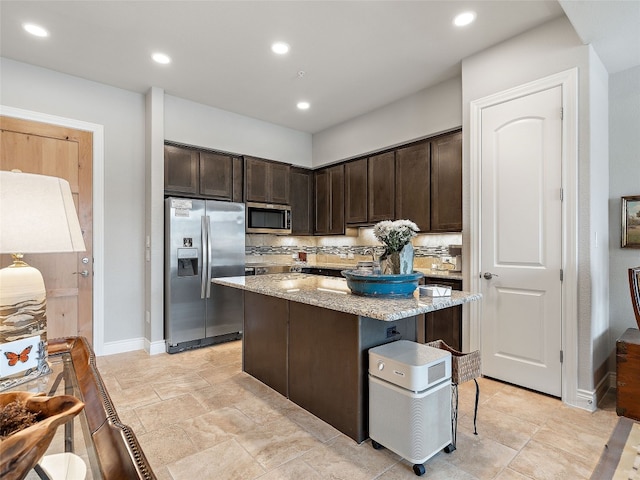 kitchen featuring a kitchen island, dark brown cabinets, appliances with stainless steel finishes, a breakfast bar, and decorative backsplash