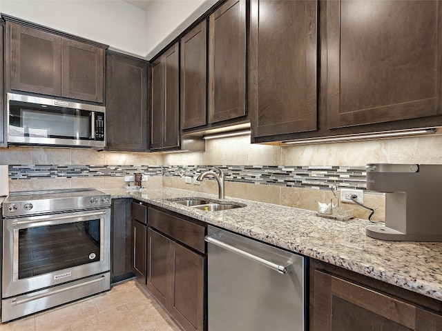 kitchen with stainless steel appliances, sink, decorative backsplash, light stone counters, and dark brown cabinetry