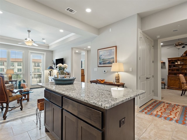 kitchen with a center island, light stone countertops, ceiling fan, a tray ceiling, and dark brown cabinetry