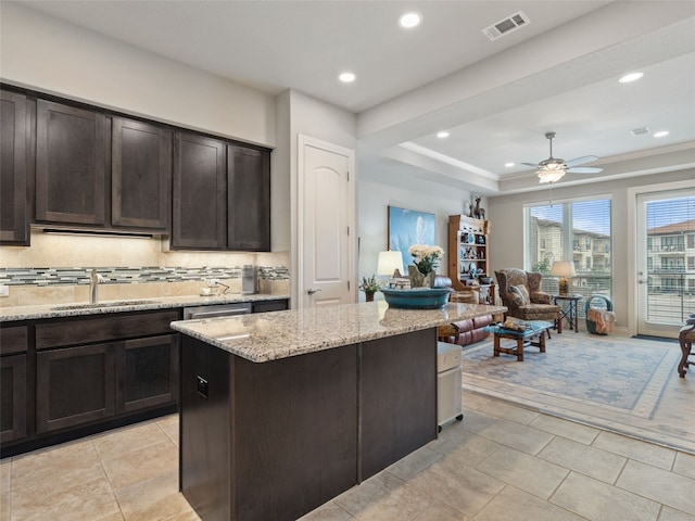 kitchen with a kitchen island, backsplash, sink, ceiling fan, and light stone counters