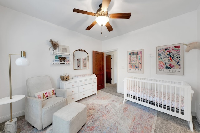 carpeted bedroom with ceiling fan and a nursery area