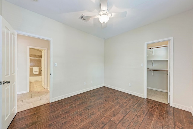 unfurnished bedroom featuring ceiling fan, a walk in closet, a closet, and dark hardwood / wood-style flooring