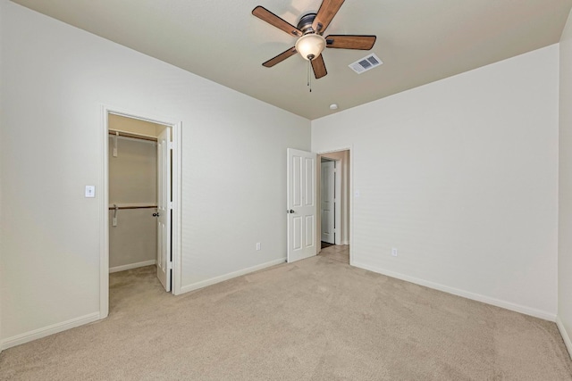 unfurnished bedroom featuring light carpet, a spacious closet, ceiling fan, and a closet