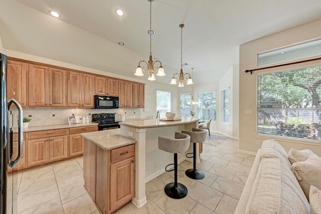 kitchen featuring hanging light fixtures, black appliances, a center island, light stone countertops, and an inviting chandelier