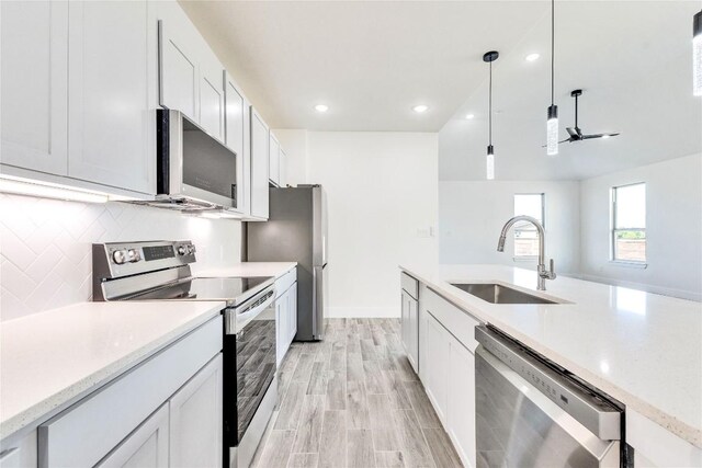 kitchen with decorative light fixtures, light wood-type flooring, appliances with stainless steel finishes, white cabinetry, and sink